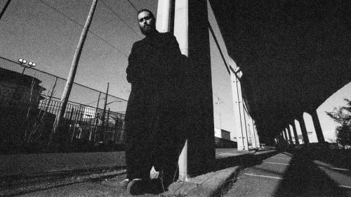 Nick Hakim is pictured from below in black & white, leaning against a pillar outside